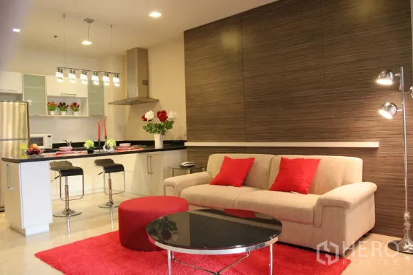 คอนโด ให้เช่าในKhlong Toei, Bangkok - ห้องนั่งเล่นแบบเปิดโล่ง โซฟาสีครีมหมอนแดง พร้อมครัวสมัยใหม่และเคาน์เตอร์บาร์