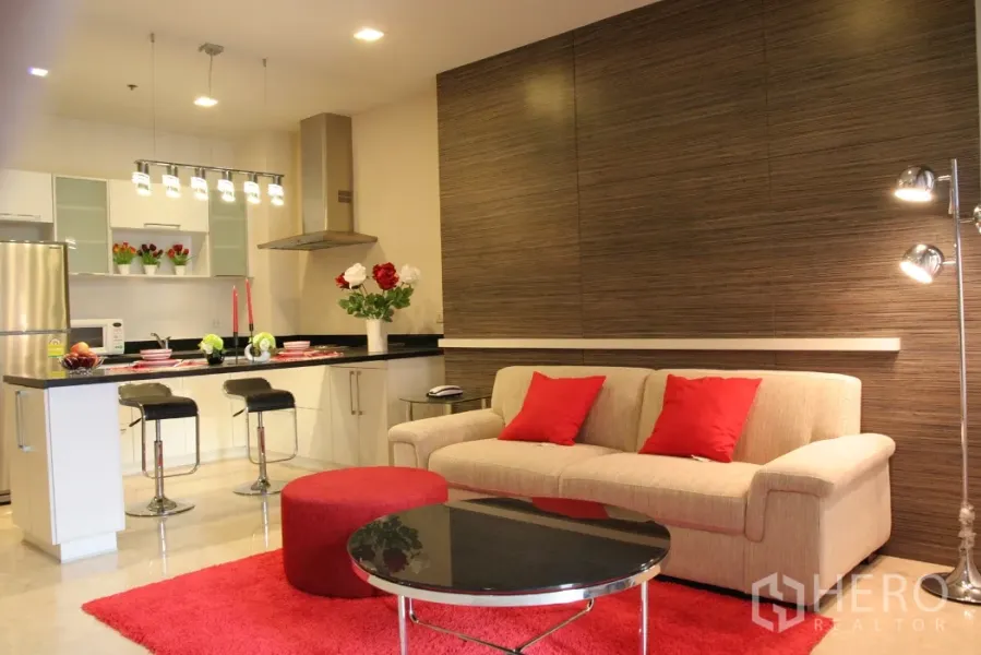 คอนโด ให้เช่าในKhlong Toei, Bangkok - ห้องนั่งเล่นแบบเปิดโล่ง โซฟาสีครีมหมอนแดง พร้อมครัวสมัยใหม่และเคาน์เตอร์บาร์