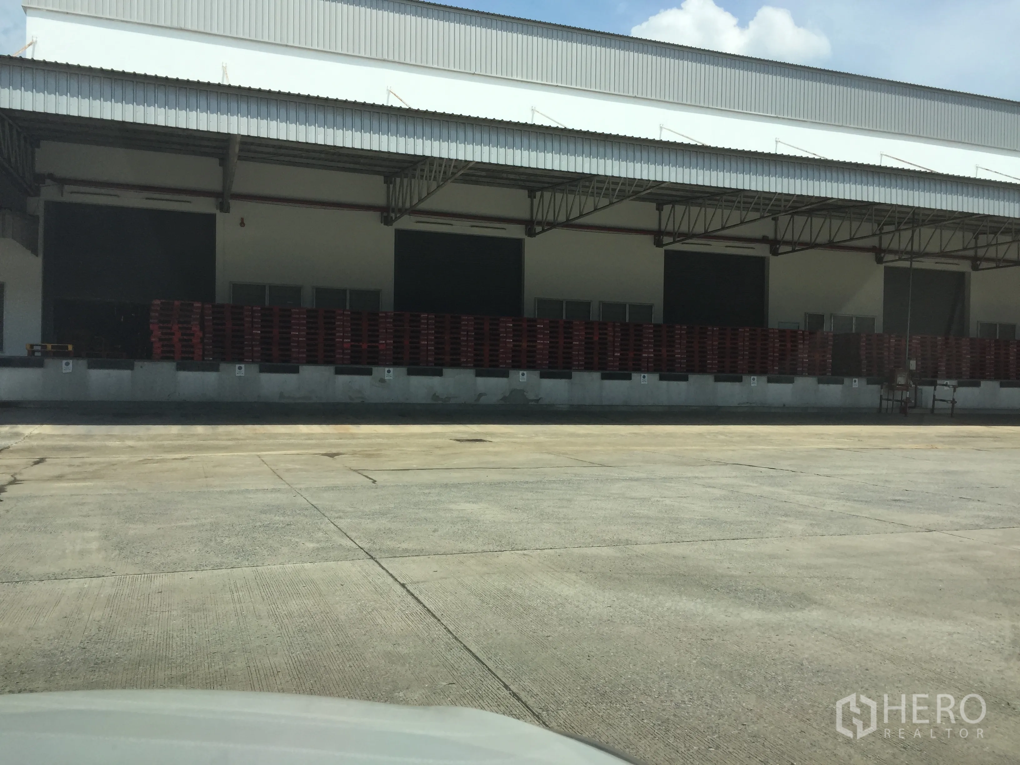 货栈 出租在Khlong Luang, Pathum Thani - 近景：多扇卷帘装卸门、整齐堆放的托盘以及宽阔的混凝土车场。