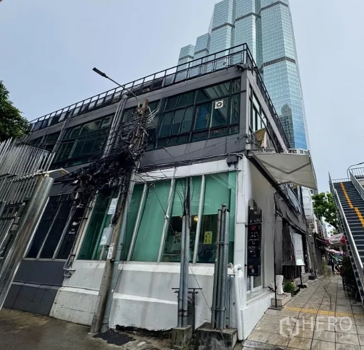 Shophouse for rent in Sathon, Bangkok - Corner two-storey building exterior with glass windows beside a pedestrian stairway.