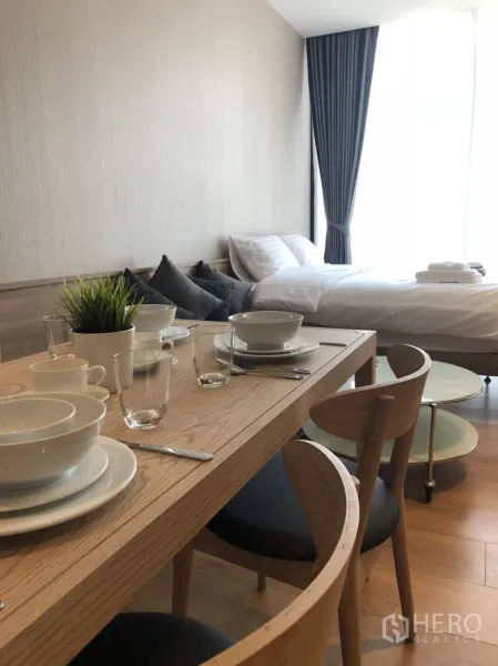 Condominium for rent in Khlong Toei, Bangkok - Cozy sleeping area beside a large window with a dining set for two in a modern condo.