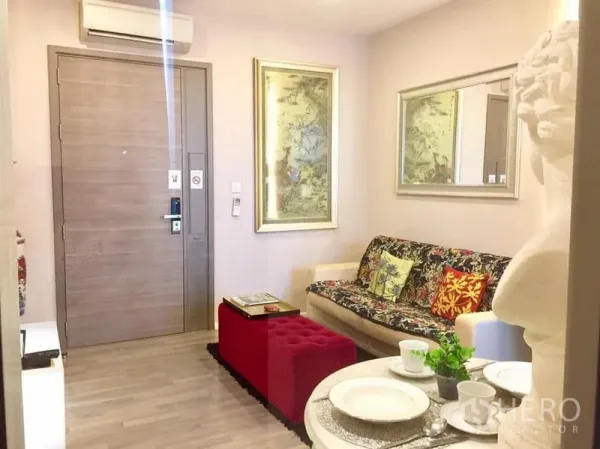 公寓 出租或出售在Watthana, Bangkok - 客厅配花纹沙发、红色脚凳、大镜面与木质入户门。