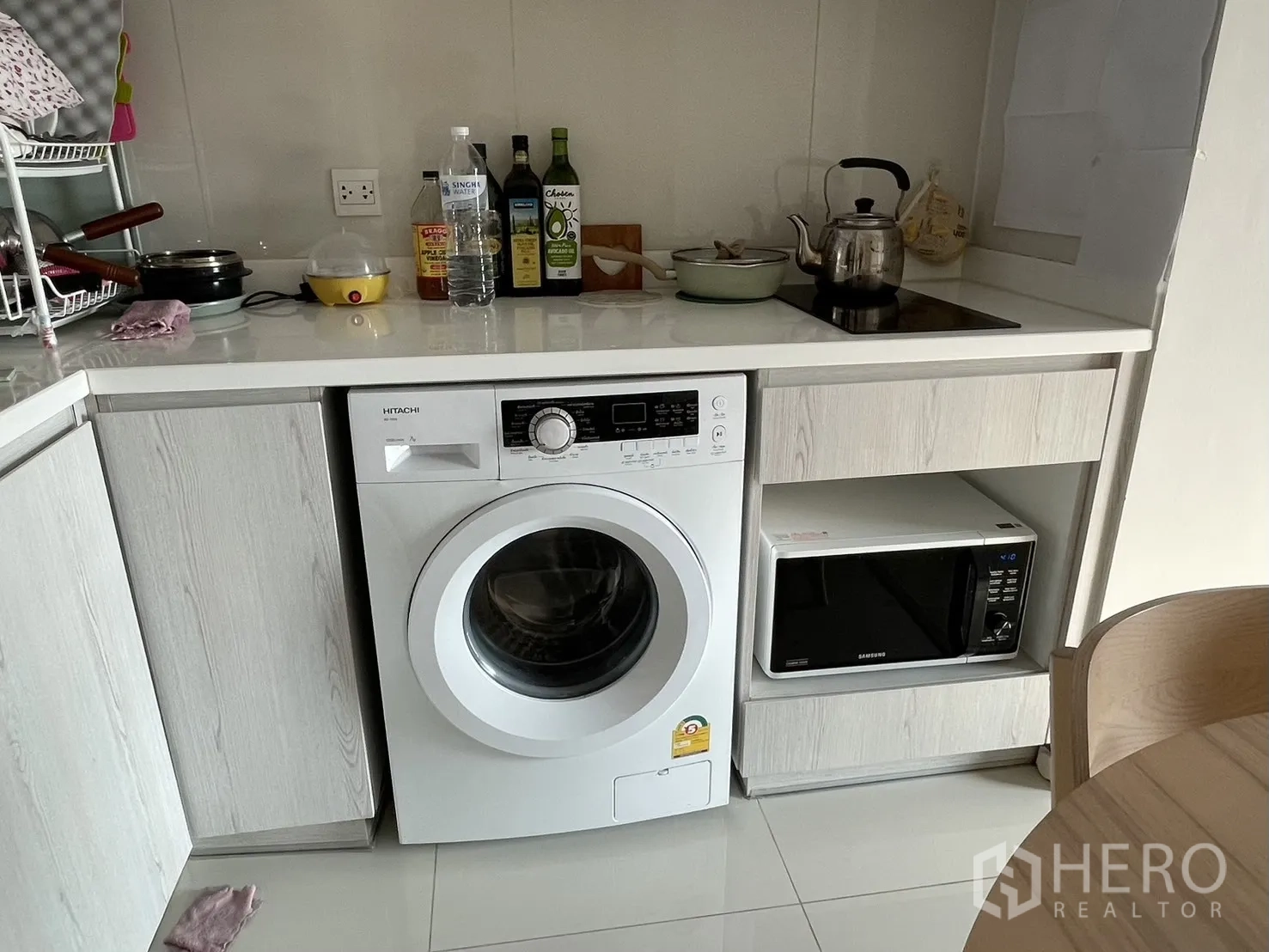 Condominium for rent in Pathum Wan, Bangkok - Compact L-shaped kitchen with built-in washer, microwave and induction cooktop under white cabinetry.