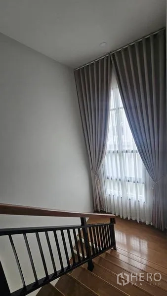 Detached House for rent in Bang Bo, Samut Prakan - Staircase with wooden steps and tall window with curtains.