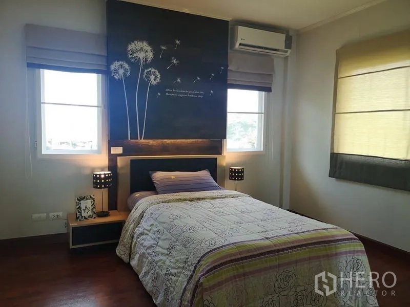 บ้าน ให้เช่า - ห้องนอนมุมบ้าน ผนังลายดอกไม้ โคมไฟหัวเตียง เครื่องปรับอากาศ และหน้าต่างคู่