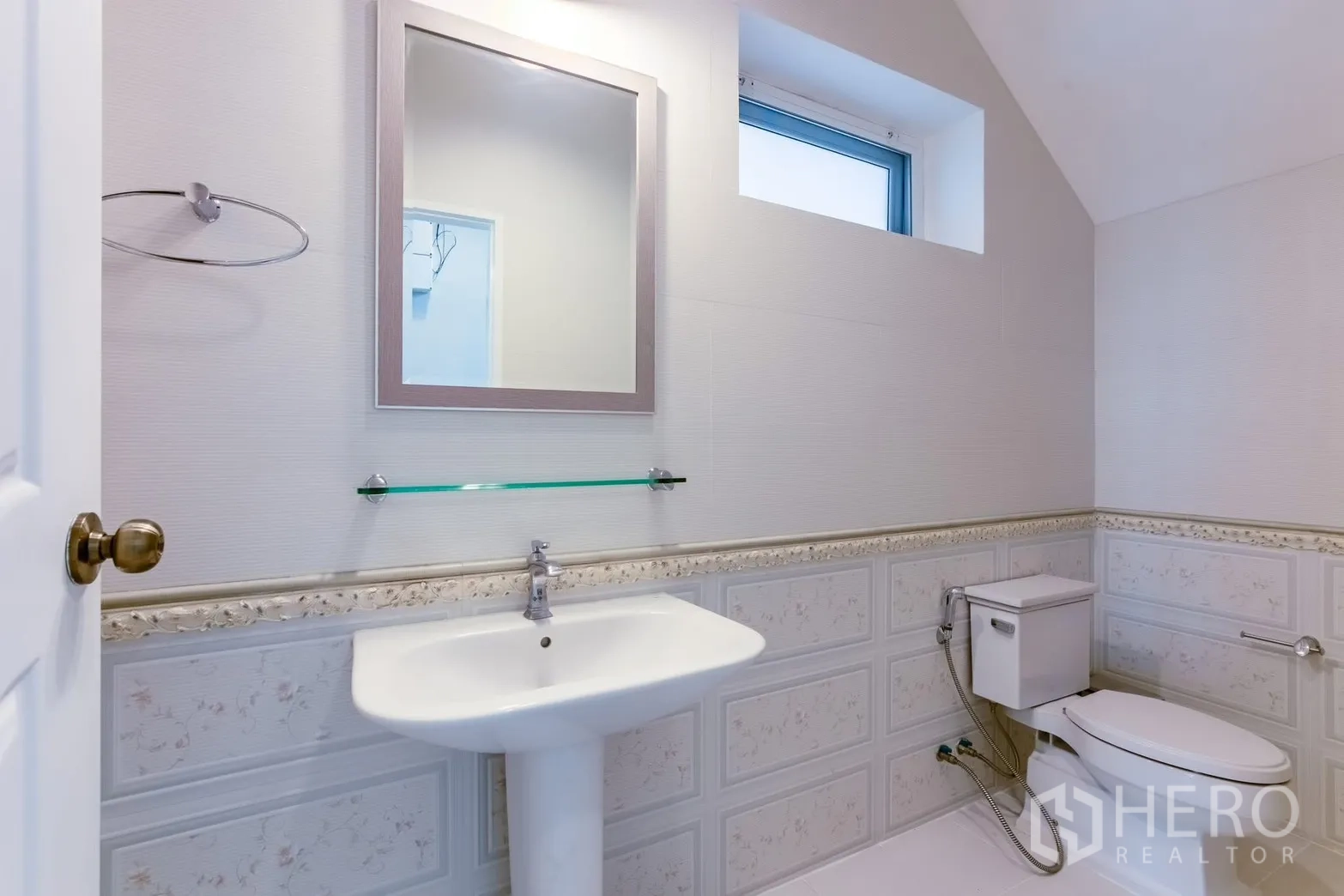 Detached House for rent in Bang Na, Bangkok - Bright bathroom with pedestal sink, wall mirror, and toilet beneath a small window.