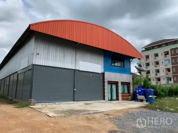 货栈 出售在Lam Luk Ka, Pathum Thani - Lam Luk Ka仓库外观，红色拱形屋顶、多个灰色卷帘门，带前置办公室与蓝色蓄水罐及混凝土装货区。