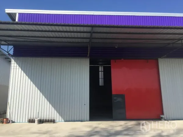 Warehouse for rent in Sai Mai, Bangkok - Metal-clad warehouse facade in Sai Mai with purple fascia, deep canopy and a large red sliding door.