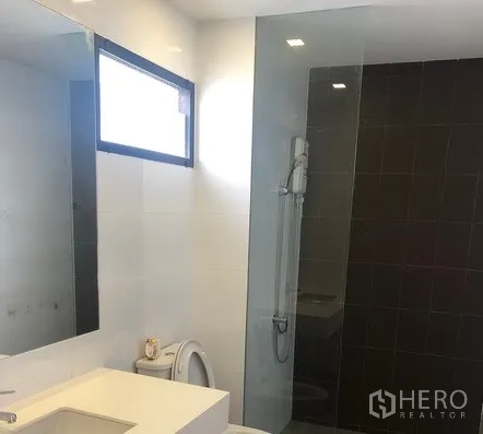 Townhouse for rent in Saphan Sung, Bangkok - Modern bathroom with large mirror, vanity, toilet and glass-enclosed shower.