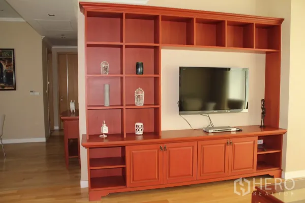 คอนโด ให้เช่าในKhlong Toei, Bangkok - ห้องนั่งเล่นตู้บิลท์อินไม้สีแดงพร้อมชั้นวางและทีวีติดผนัง พื้นไม้จริง
