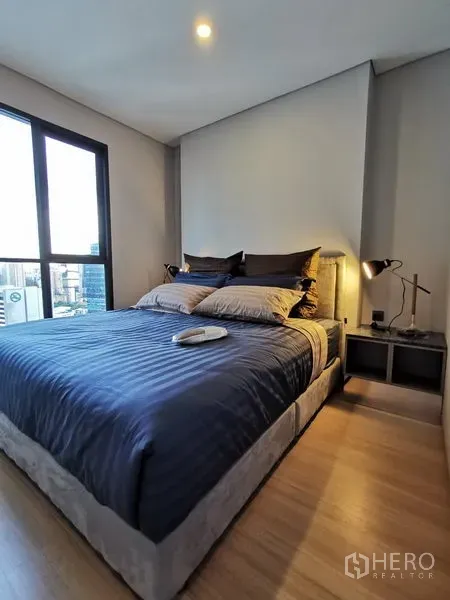 Condominium for rent in Ratchathewi, Bangkok - Cozy 1-bedroom Ratchathewi condo bedroom with double bed, bedside lamps, wood flooring and large city-view window.