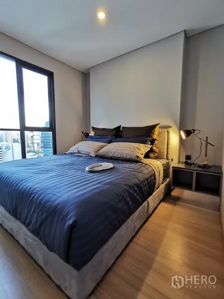 Condominium for rent in Ratchathewi, Bangkok - Cozy 1-bedroom Ratchathewi condo bedroom with double bed, bedside lamps, wood flooring and large city-view window.