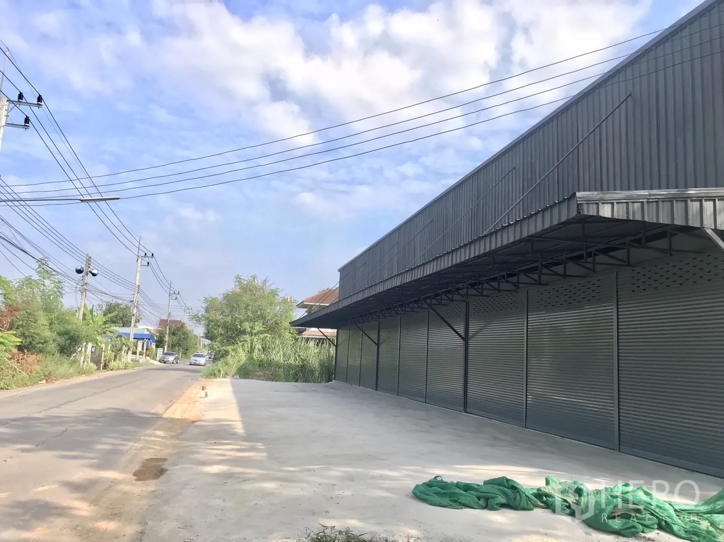 คลังสินค้า ให้เช่าในLam Luk Ka, Pathum Thani - มุมมองด้านข้างของโกดังผนังเมทัลชีทติดถนนท้องถิ่นพร้อมพื้นที่จอดกว้าง