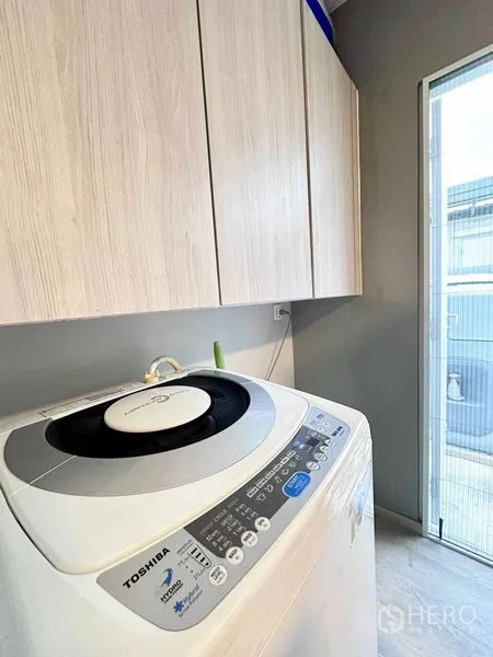 独立式住宅 出租或出售在Prawet, Bangkok - 洗衣区，波轮洗衣机与顶柜，旁有后门。