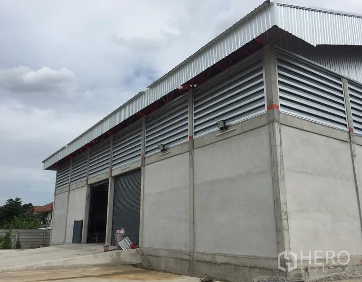 Warehouse for rent in Khlong Sam Wa, Bangkok - Modern warehouse exterior with concrete walls, louver vents, a loading ramp, and a large roller shutter door.