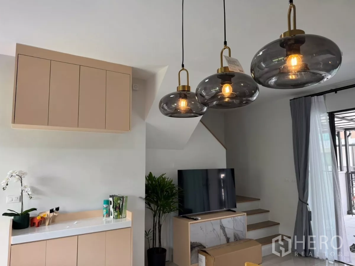 Townhouse for rent in Bang Phli, Samut Prakan - Living area with trio of pendant lights, TV console, and staircase