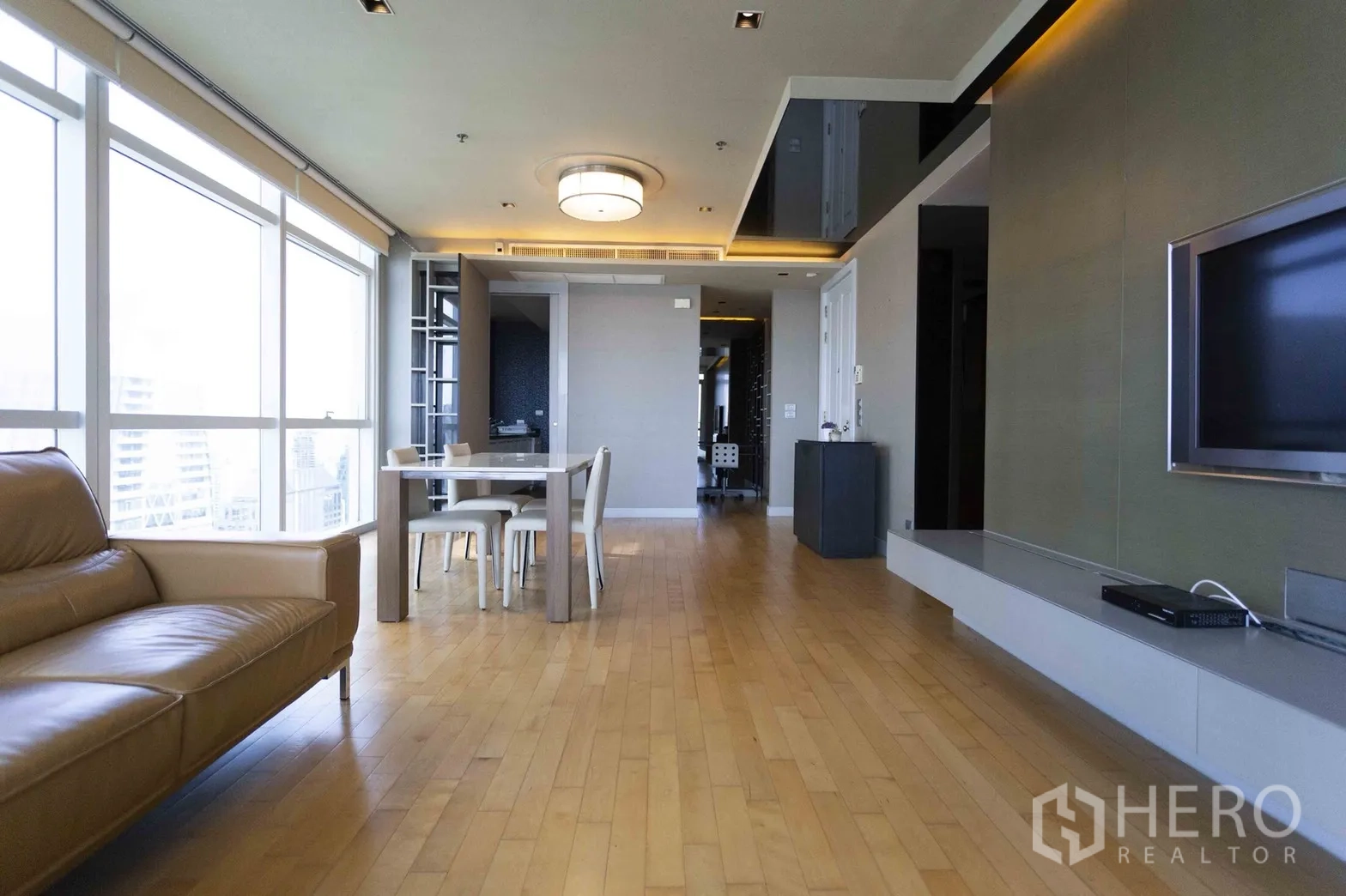 Condominium for rent in Pathum Wan, Bangkok - Dining area beside large windows with neutral decor and wood flooring in a modern condo.
