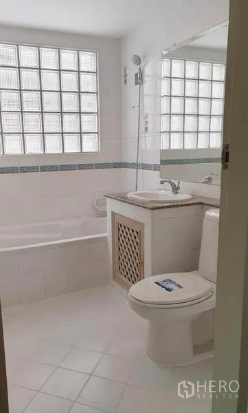 Detached House for rent in Huai Khwang, Bangkok - White bathroom with bathtub, glass-block window, vanity and toilet.