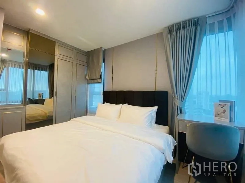 คอนโด ให้เช่า - ห้องนอนหลักมีตู้เสื้อผ้าบานกระจก โต๊ะทำงานริมหน้าต่าง และหัวเตียงบุนวม