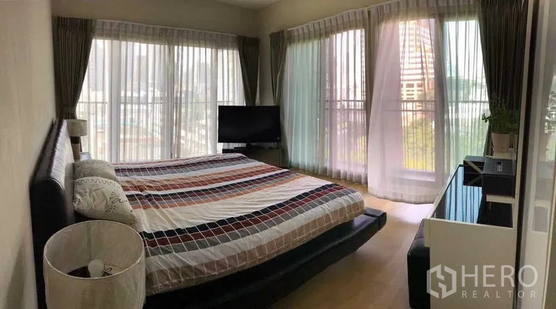 Condominium for rent in Watthana, Bangkok - Corner master bedroom with panoramic windows, city view, and a king-size bed.