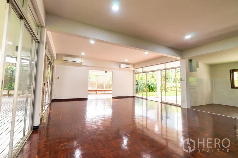 Detached House for rent in Khlong Toei, Bangkok - Open‑plan living area with polished wood floors and floor‑to‑ceiling sliding glass doors facing the garden.