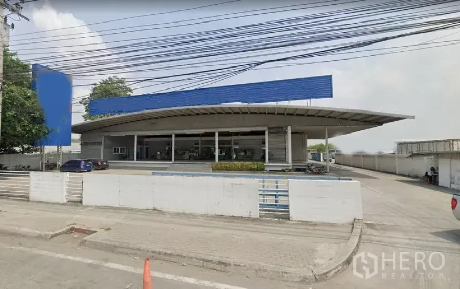 Warehouse for rent in Bang Phli, Samut Prakan - Street-side view of a modern Bang Phli warehouse with a large curved canopy, gated entrance, and wide driveway.