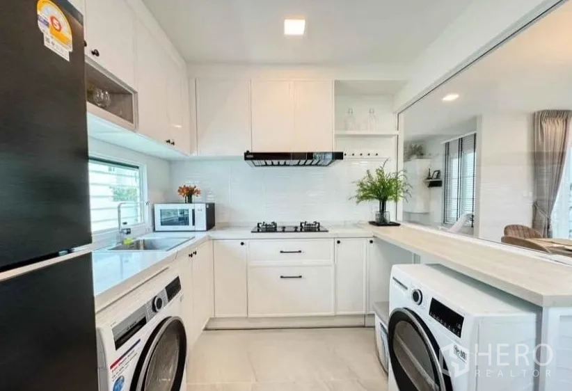 Detached House for rent in Bang Phli, Samut Prakan - Compact white kitchen with gas hob, fridge and stacked washer dryer.
