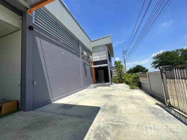 โรงงาน ขายในLam Luk Ka, Pathum Thani - ด้านหน้าโรงงานสมัยใหม่ติดถนนทางเข้า พร้อมรั้วประตู.