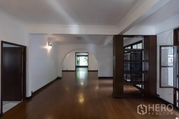Detached House for rent in Pathum Wan, Bangkok - Long living area with built-in shelving, wooden floors and garden view through arch.