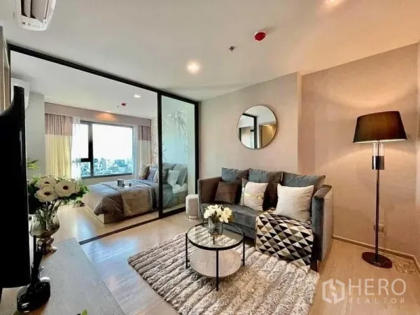 Condominium for rent in Chatuchak, Bangkok - Open-plan living room with round wall mirror, textured rug and glass wall to bedroom.