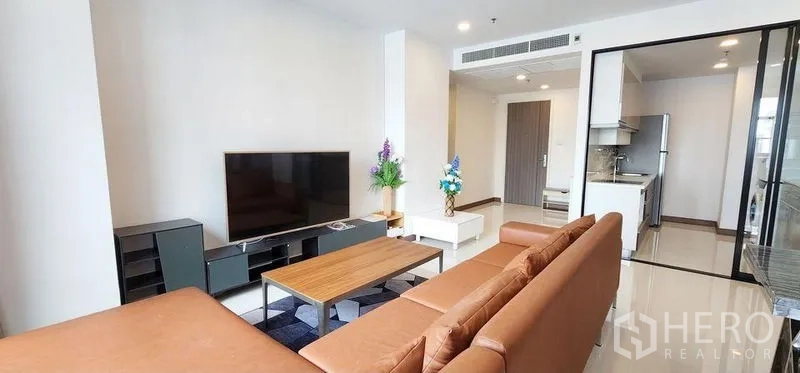 Condominium for rent - Open-plan lounge facing a large flat-screen TV with a glass-partitioned kitchen beyond.