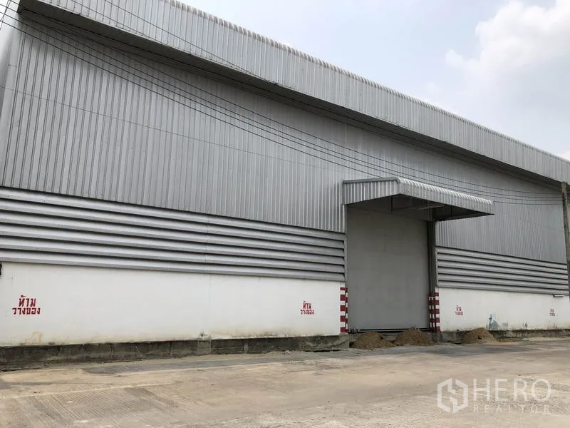 Warehouse for rent in Pathum Thani - Close view of the warehouse facade with a big roller shutter door, metal awning and striped cladding.