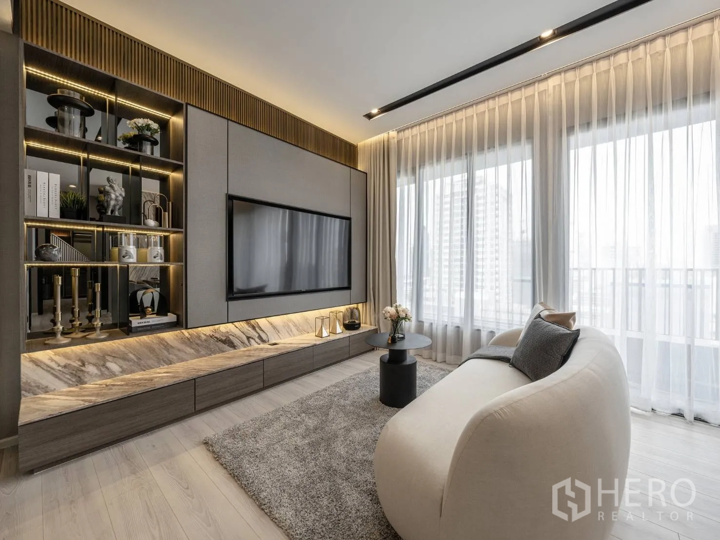 公寓 出售在Ratchathewi, Bangkok - 时尚电视墙，开放式灯光展示架与大理石台面，弧形沙发面向阳台。