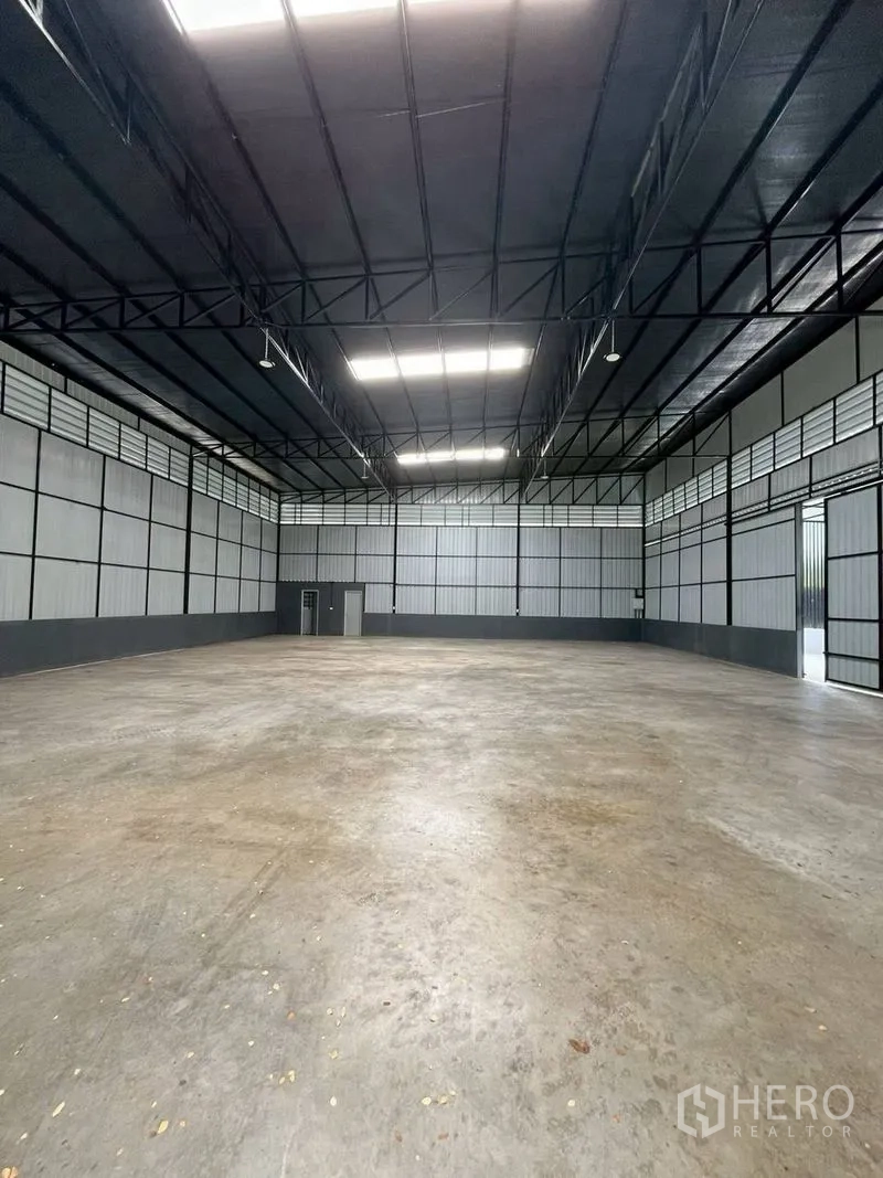 Warehouse for rent in Chatuchak, Bangkok - Spacious warehouse interior with a high steel truss roof, skylights, and a smooth concrete floor.