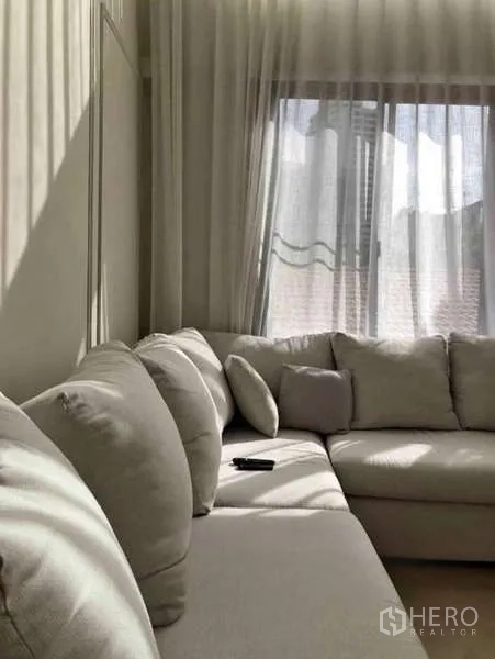 Townhouse for rent - Close-up of a beige sectional sofa beside a window with sheer drapes.