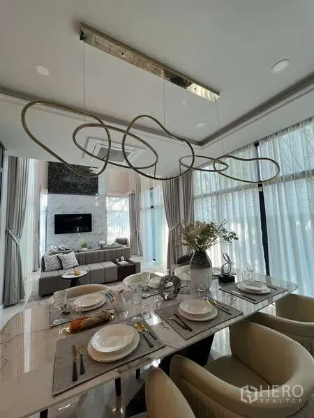 Detached House for sale in Suan Luang, Bangkok - Bright open-plan dining and living room with marble table, statement chandelier and floor-to-ceiling curtains