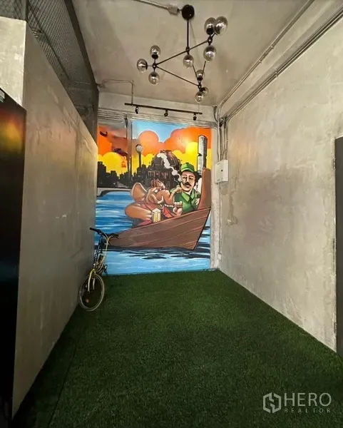 零售空间 出租在Watthana, Bangkok - 狭长室内通道，铺人造草坪与吊灯，尽端为墙面彩绘