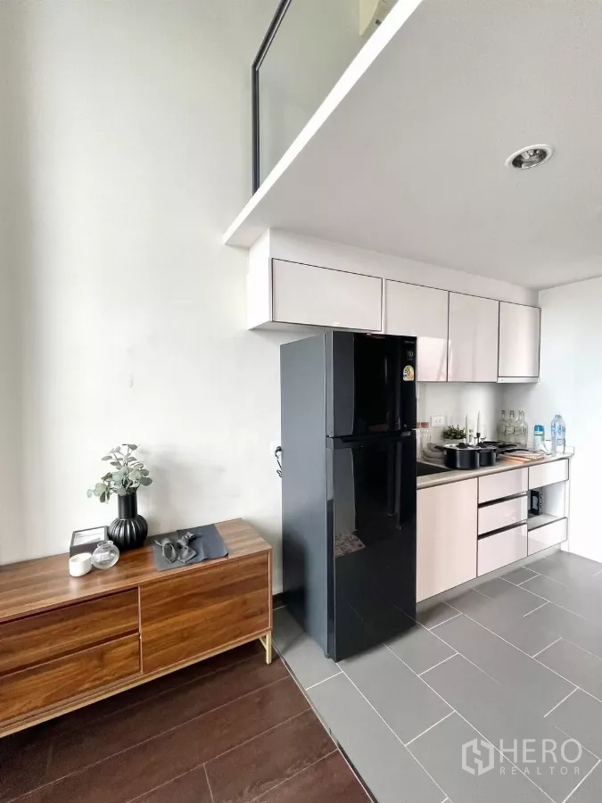 Condominium for rent in Watthana, Bangkok - Compact kitchen with upper cabinets and black fridge beside a wooden sideboard.