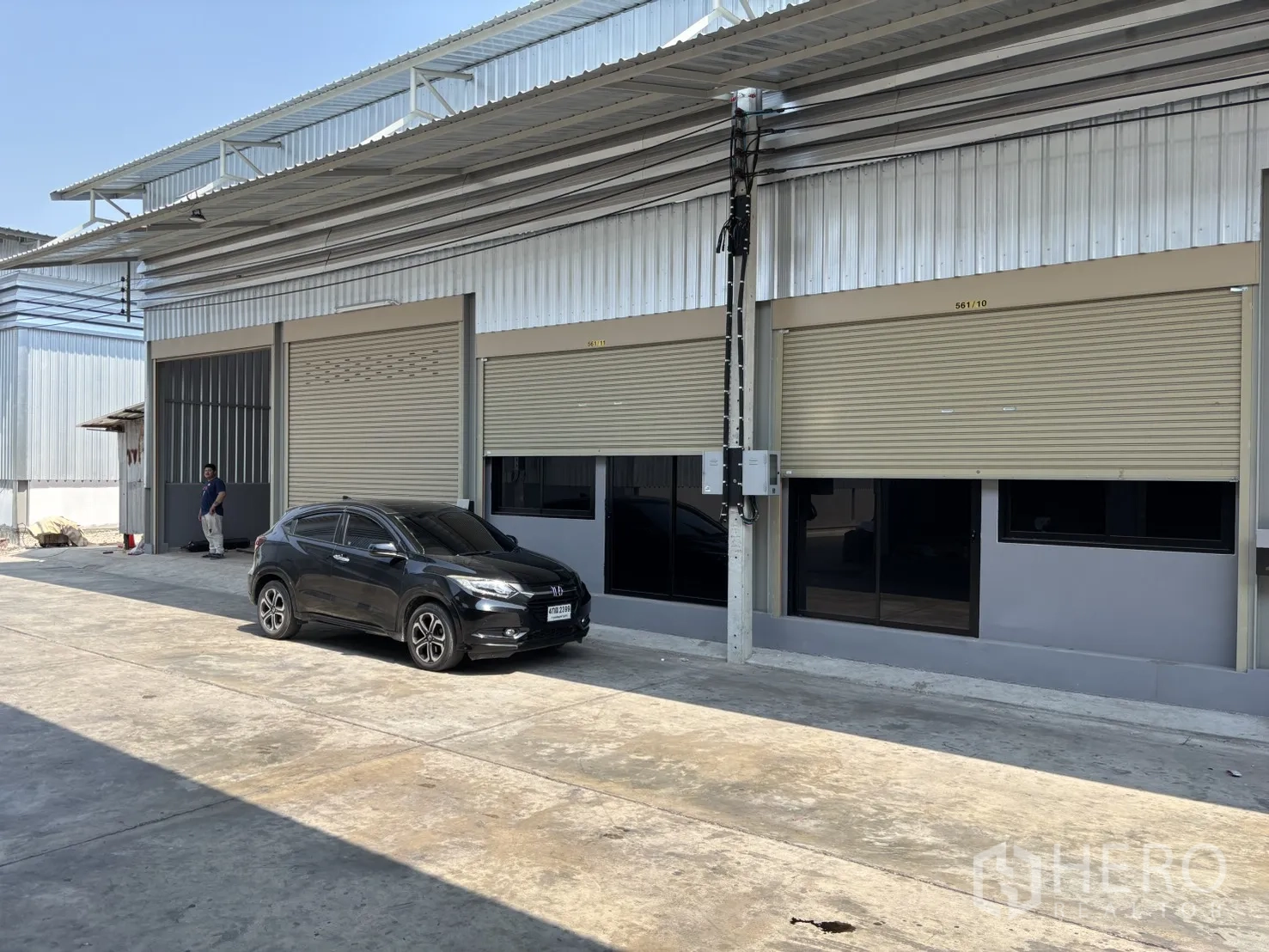 โกดัง for rent in Phra Samut Chedi, Samut Prakan - ด้านหน้าโกดังมีประตูม้วนหลายบาน กระจกด้านหน้า และพื้นที่จอดรถบนลานคอนกรีต