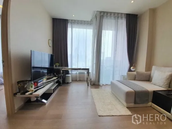 คอนโด ให้เช่าหรือขายในWatthana, Bangkok - ห้องนั่งเล่นสว่าง ผนังกระจกสูงจรดเพดาน พร้อมชั้นวางทีวีและโต๊ะทำงาน ติดระเบียงวิวเมือง