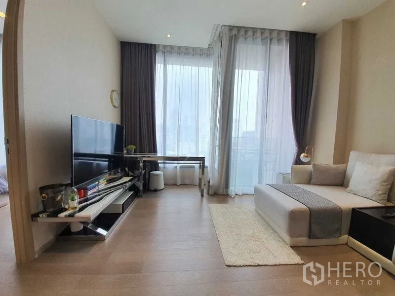 คอนโด ให้เช่าหรือขายในWatthana, Bangkok - ห้องนั่งเล่นสว่าง ผนังกระจกสูงจรดเพดาน พร้อมชั้นวางทีวีและโต๊ะทำงาน ติดระเบียงวิวเมือง