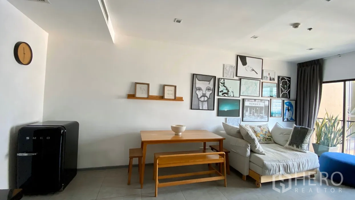 คอนโด ให้เช่าในBangkok - ห้องนั่งเล่นสว่าง กำแพงแกลเลอรี โต๊ะอาหารไม้ ม้านั่ง โซฟา และระเบียงมีต้นไม้ในคอนโดสไตล์โมเดิร์น