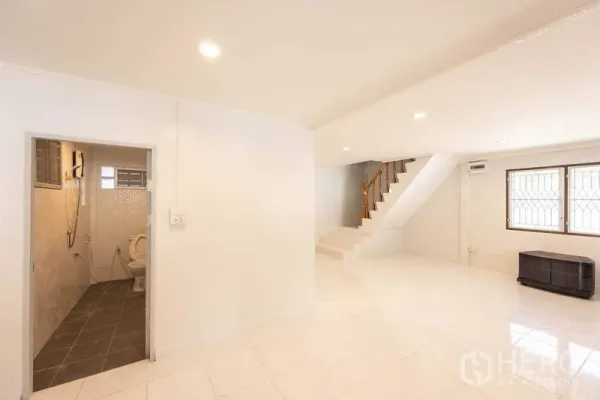 Home Office for rent in Watthana, Bangkok - Bright ground floor with white tiles, staircase, and bathroom—ideal for reception or work area.
