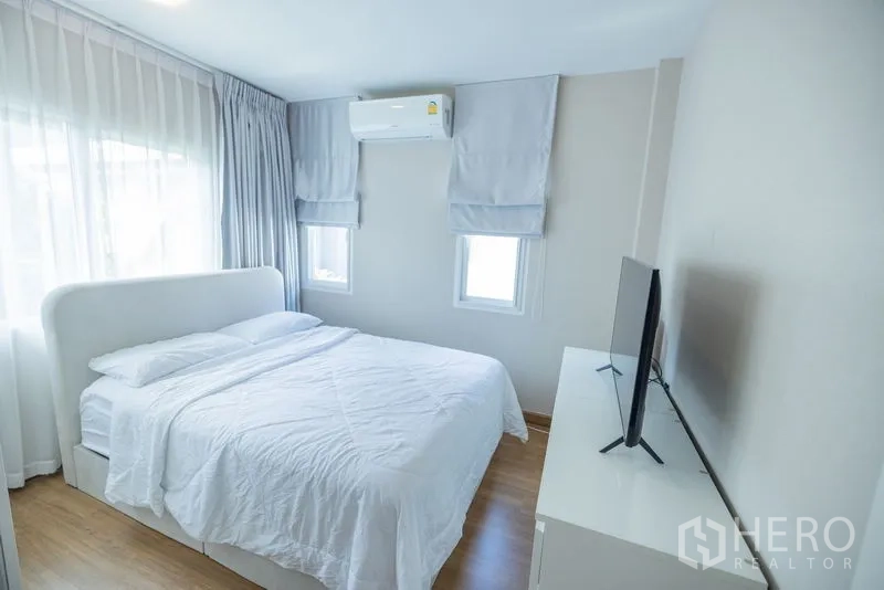 Detached House for rent or sale in Bang Phli, Samut Prakan - Airy bedroom with white bed, TV on dresser and double windows with curtains.