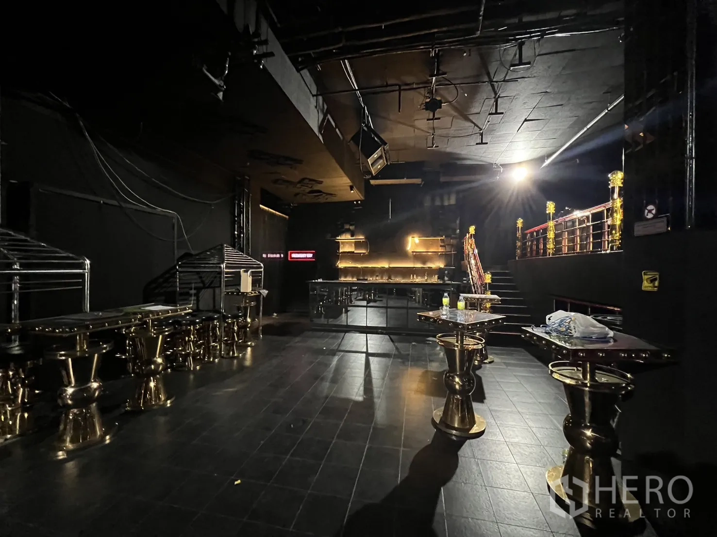 零售空间 出租 - 主层设有背光吧台、金色高脚桌和通往夹层的楼梯。