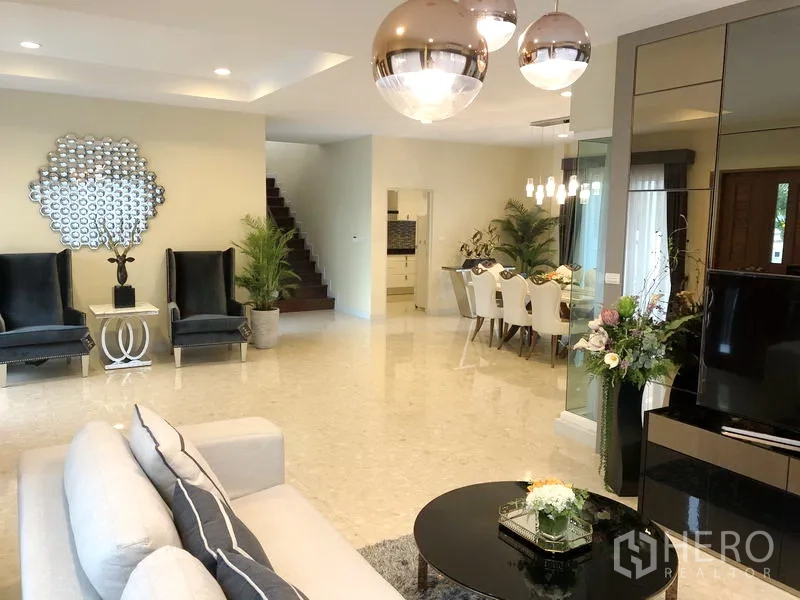 Detached House for rent or sale in Saphan Sung, Bangkok - Open-plan living area with polished floors, feature chairs, staircase and modern pendant lighting.