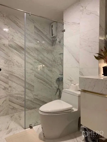 คอนโด ขายในKhlong Toei, Bangkok - ห้องน้ำที่สอง ผนังหินอ่อนสีขาว ฝักบัวกั้นกระจก เคาน์เตอร์อ่างล้างหน้า และโถสุขภัณฑ์