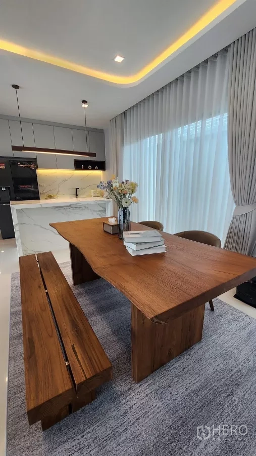 บ้าน ให้เช่าหรือขายในBueng Kum, Bangkok - โต๊ะทานข้าวไม้สักบนพรม ข้างผ้าม่านโปร่งและไฟซ่อนลายเพดาน