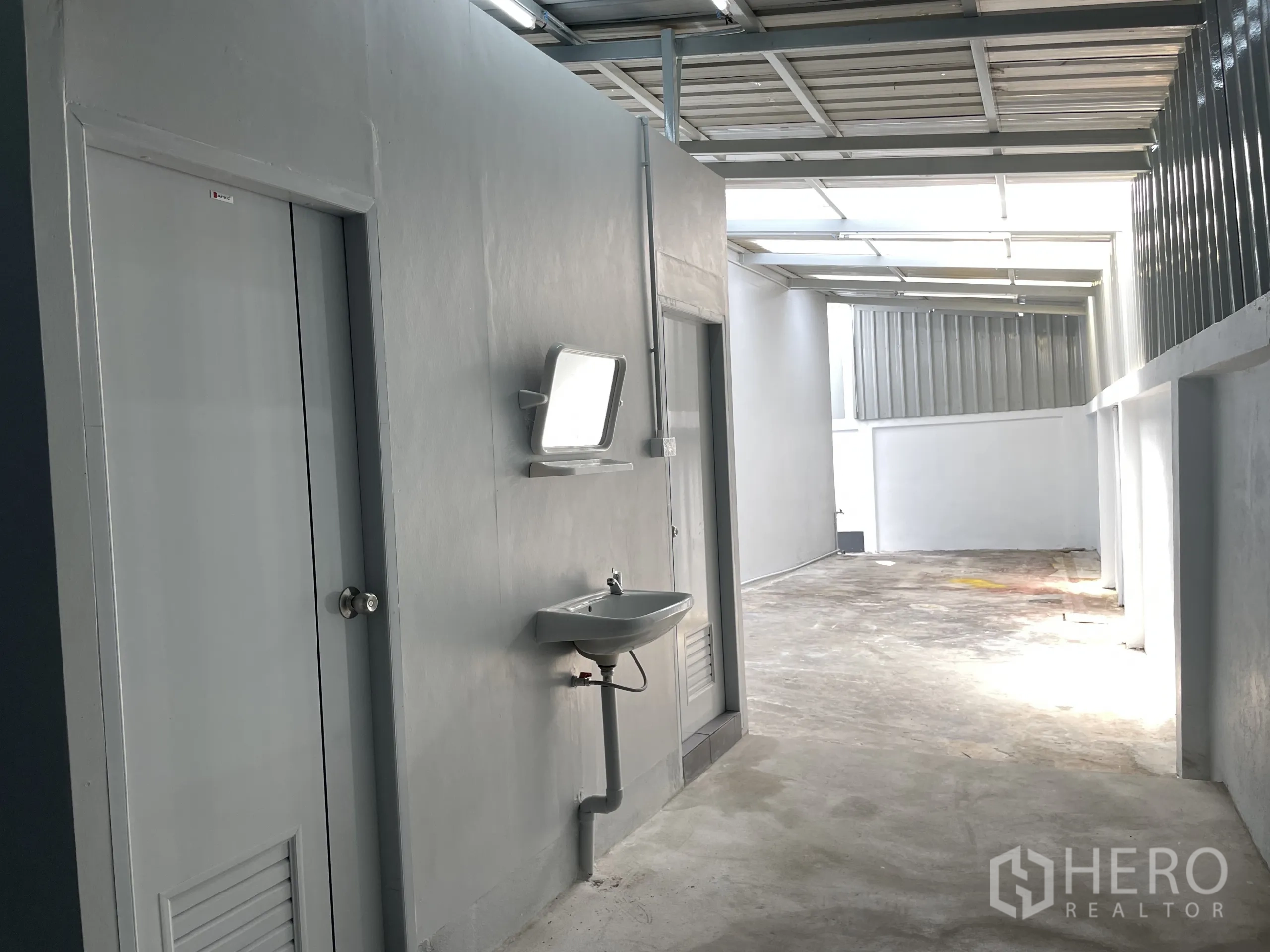 Factory for rent in Ban Phaeo, Samut Sakhon - Rear service area showing restrooms, a wall-mounted sink and covered walkway.