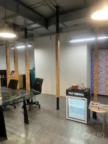 Office Space for rent - Glass meeting table beside a self-service refreshment fridge within a pillar-lined workspace.